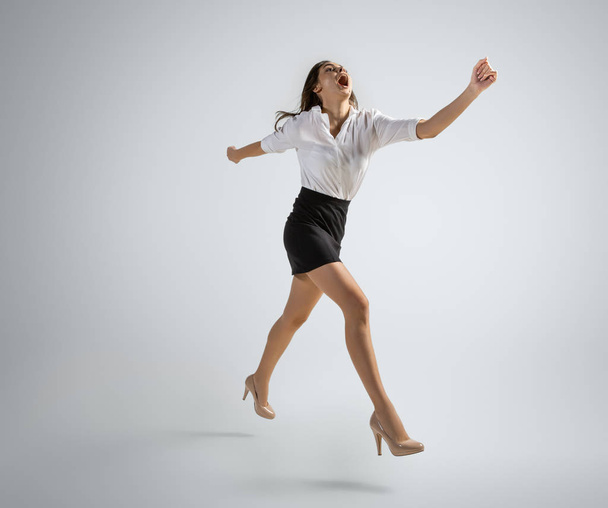 Caucasian woman in office clothes running isolated on grey studio background - Foto, Imagem