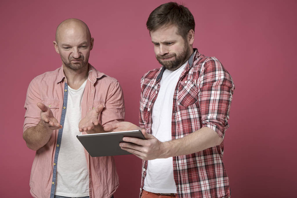 Two displeased men are looking at the tablet, they are disappointed with what they saw and are upset. - Photo, Image