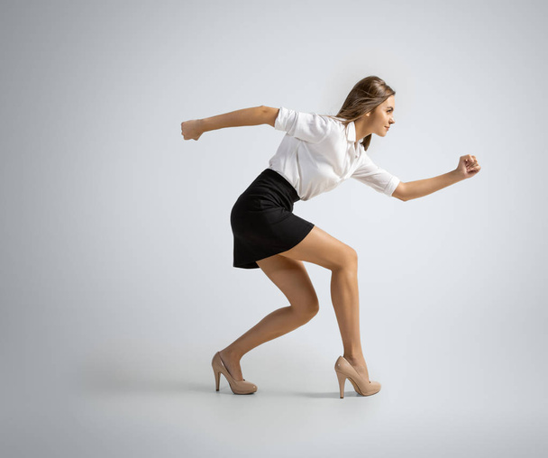 Caucasian woman in office clothes preparing to run isolated on grey studio background - Foto, afbeelding