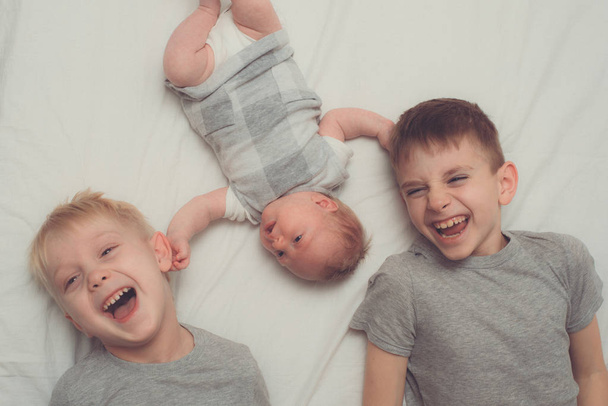 Dva starší bratři a nejmladší dítě v bílé posteli. Šťastné dětství, velká rodina. Horní pohled - Fotografie, Obrázek