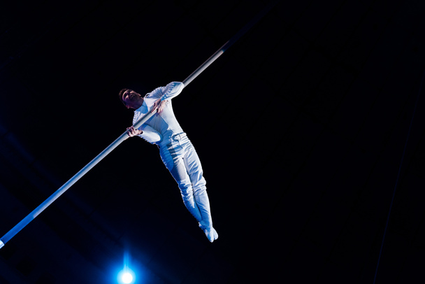 visão de baixo ângulo do homem balanceamento enquanto segurando pólo metálico na arena de circo
  - Foto, Imagem