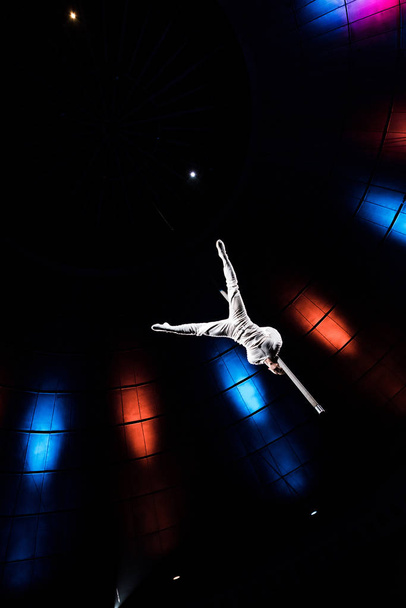 low angle view of athletic acrobat balancing on metallic pole in arena of circus  - Фото, зображення