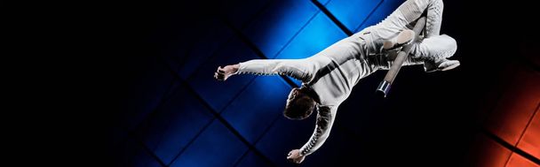 panoráma felvétel akrobata kiegyensúlyozó fém rúd közelében kék és piros világítás cirkuszban  - Fotó, kép