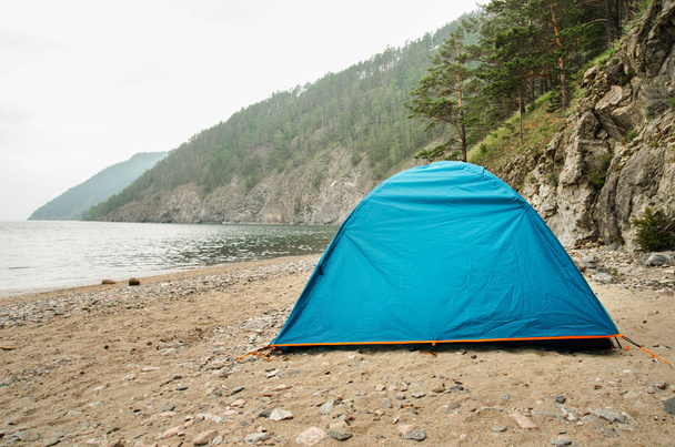 Голубая палатка стоит в горах на скалах у озера
 - Фото, изображение