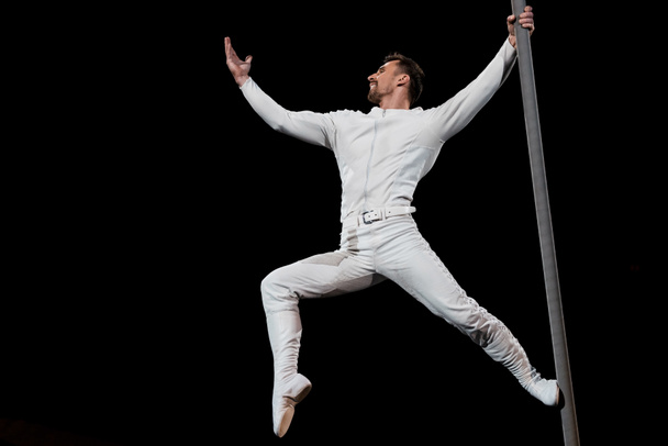 strong acrobat posing while performing and holding metallic pole isolated on black  - Фото, изображение