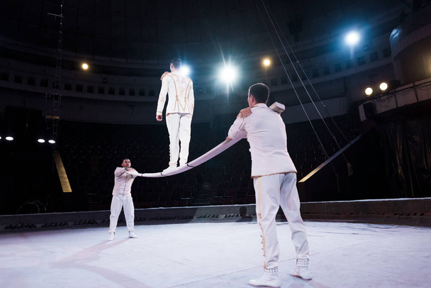 acrobats supporting man walking on metallic pole in circus - Фото, зображення