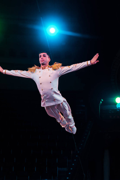 handsome air acrobat with outstretched hands flying in arena of circus  - Photo, Image