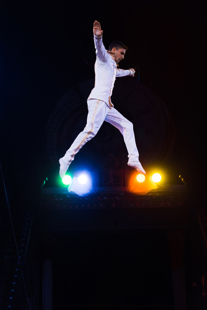 side view of handsome gymnast with outstretched hands jumping in arena of circus  - Foto, immagini