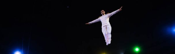 panoramic shot of handsome air acrobat with outstretched hands in arena of circus  - Photo, Image