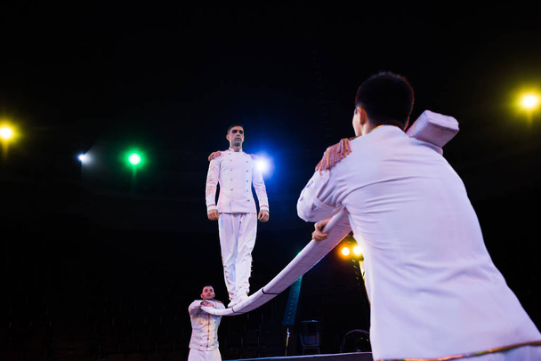 low angle view of handsome air acrobat balancing on pole near men in circus  - Photo, Image