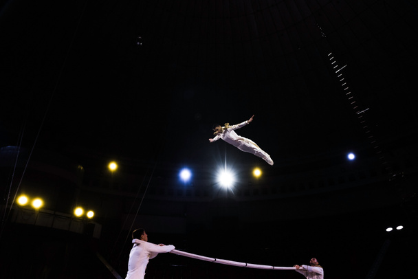 acrobata de ar pulando enquanto se apresenta perto de homens no circo
  - Foto, Imagem