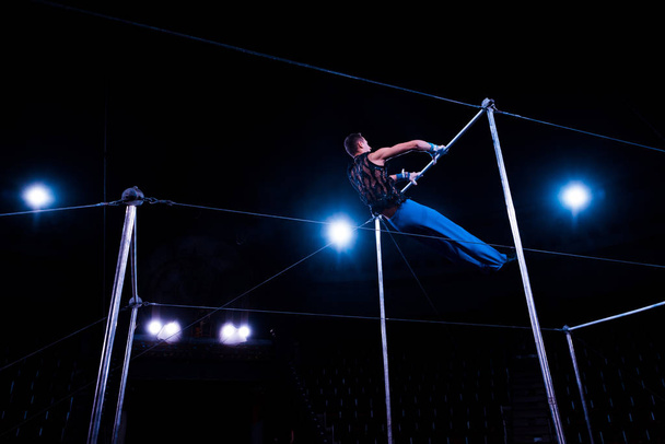 low angle view of gymnast performing on horizontal bars in arena of circus   - Foto, Imagem