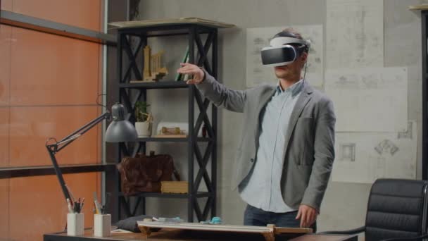 Мужчина-архитектор в офисе в шлеме виртуальной реальности использует жесты для управления проектом, не выходя из офиса. Строительный контроль. Дизайн здания и интерьера
. - Кадры, видео