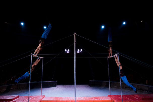 four gymnasts performing on horizontal bars in arena of circus   - Foto, Bild
