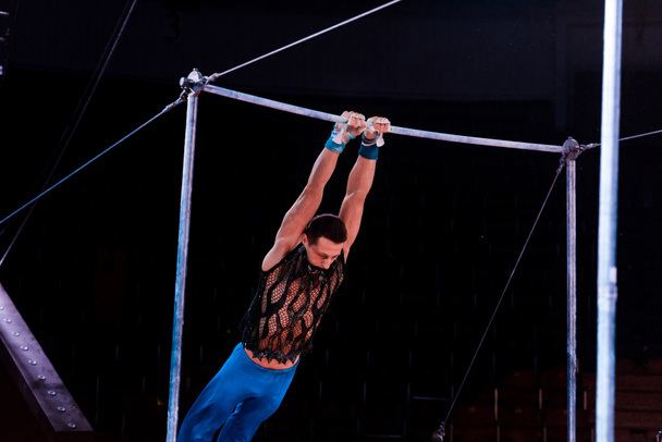 athletischer Mann, der in der Manege des Zirkus am Stufenbarren auftritt   - Foto, Bild