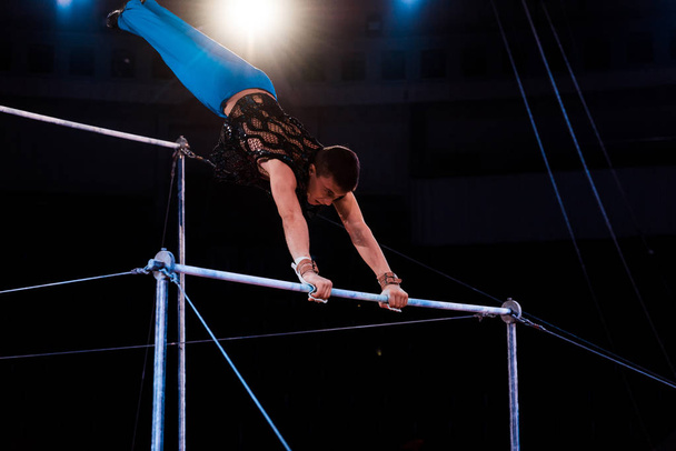athletic gymnast exercising on horizontal bars in arena of circus   - Foto, Bild