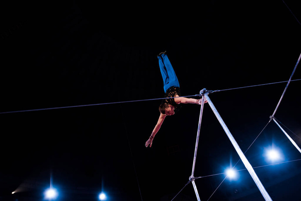 low angle view of athletic man performing on horizontal bars in arena of circus   - Foto, Bild