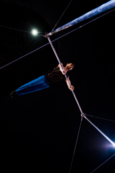 bottom view of athletic gymnast performing on horizontal bars in arena of circus   - Photo, Image