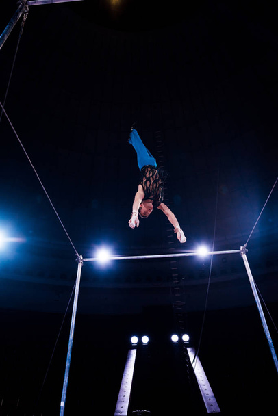  low angle view of gymnast balancing on horizontal bars in arena of circus   - Фото, изображение