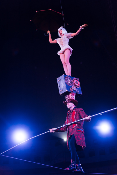 low angle view of man holding pole and supporting attractive acrobat while walking on rope  - Foto, imagen
