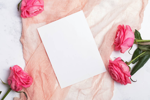Top view of blank paper card lying on the pastel color cloth on the table with pink roses. - Foto, afbeelding