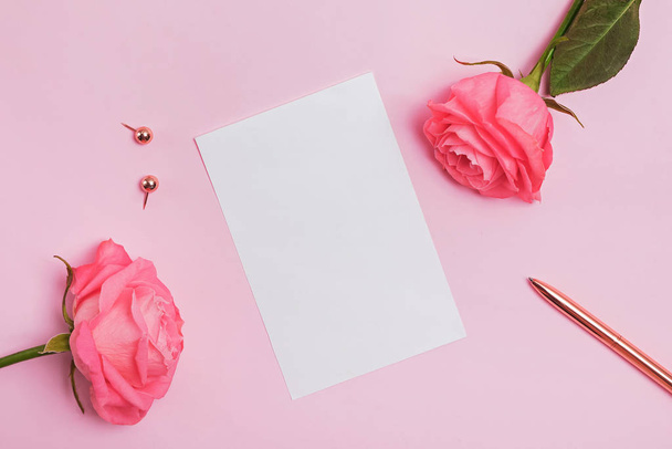 Blank paper card lying on the pink table with roses and gold color stationery. - Valokuva, kuva