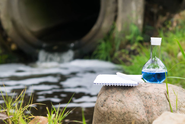 close-up of a flask with a blue reagent and a notebook with a pen against the background of the examination site - 写真・画像