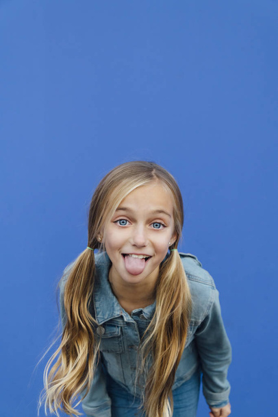 Blond meisje kijken naar camera en steken haar tong - Foto, afbeelding