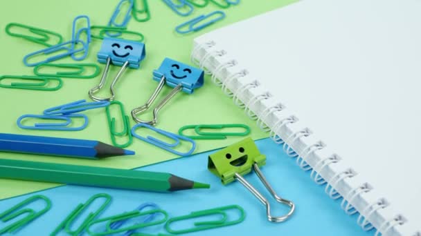 Groen en blauw kantoorpapier clip, glimlach binder clips en potloden op notitieblok - Video