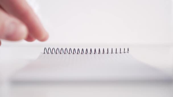 Un hombre hojea lentamente a través de un cuaderno vertical con una montura de página negra en espiral sobre un fondo blanco. Vista frontal. El concepto de utilizar el planificador en los negocios y la vida cotidiana
 - Metraje, vídeo