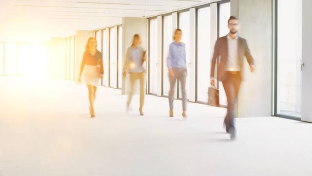 Business people walking in office hall with yellow lens flare in background - Foto, Bild