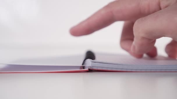 Um jovem lentamente folheia através de um caderno com páginas horizontais em espiral fixando em um fundo branco. Vista frontal. Conceito de autodisciplina usando um planejador
. - Filmagem, Vídeo