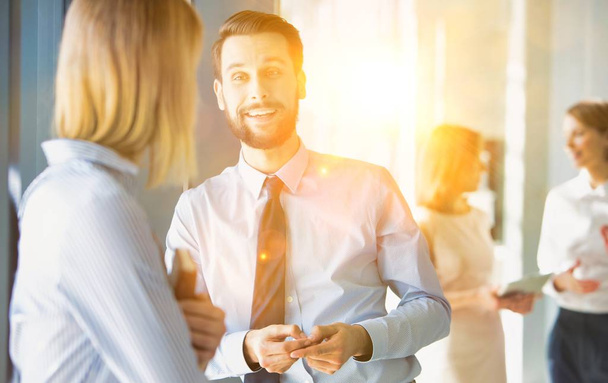 Businessman talking to businesswoman in office hall with yellow lens flare  - Foto, Imagen