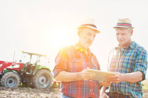 Farmers talking while using digital tablet at farm on sunny day - Φωτογραφία, εικόνα