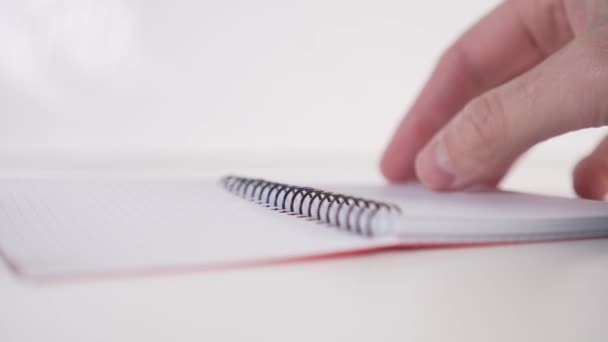 Egy fiatalember lassan átlapoz egy jegyzetfüzetet, spirális, vízszintes lapokkal, fehér háttérrel. Oldalnézetből. A tervezés és az önfegyelem fogalma - Felvétel, videó