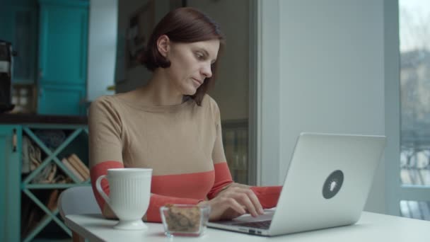 Young woman sitting at desk, taking on wireless earphones and talking online using laptop. Female talking while working on computer.  - Filmagem, Vídeo