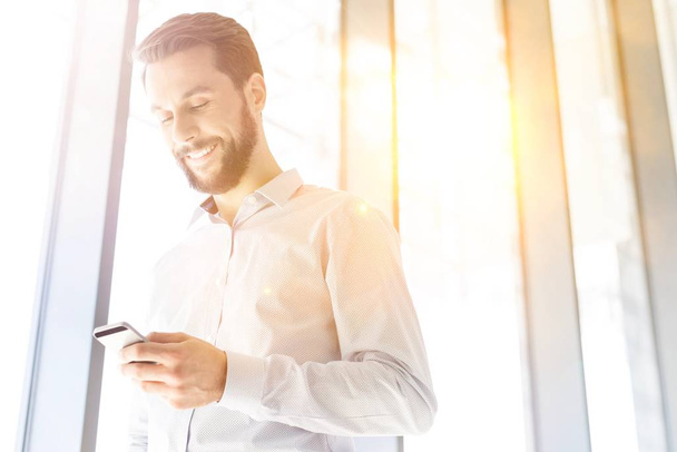 Young attractive businessman using smartphone in office hall with yellow lens flare - Photo, Image