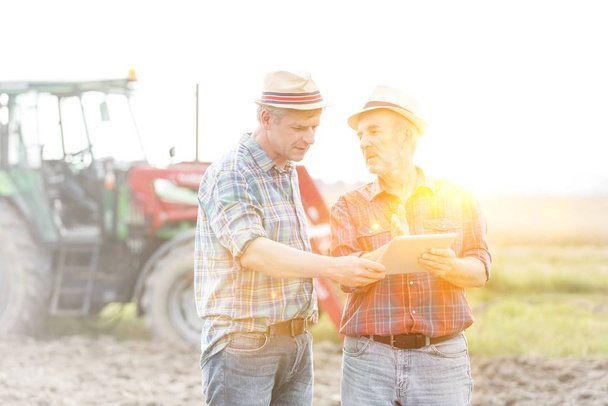 Farmers talking while using digital tablet at farm on sunny day - 写真・画像
