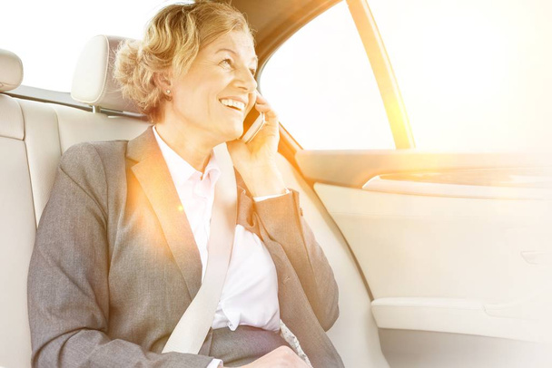 Businesswoman smiling while talking on smartphone with yellow lens flare in background  - Fotografie, Obrázek