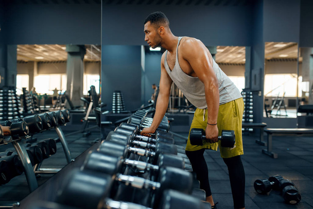М'язистий чоловік вибирає важкі гантелі для тренувань у спортзалі. Фітнес-тренування в спортивному клубі, здоровий спосіб життя, відповідні вправи
 - Фото, зображення