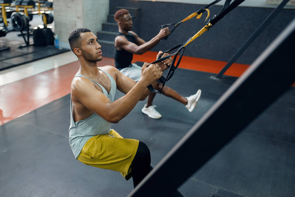 Two athletes in sportswear at exercise machine on training in gym. Fit workout in sport club, healthy lifestyle, fitness - Photo, image