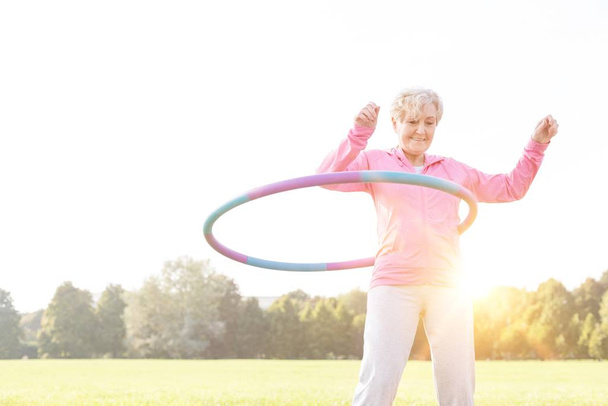 Senior woman doing gymnastic with hula hoop in park - Foto, imagen