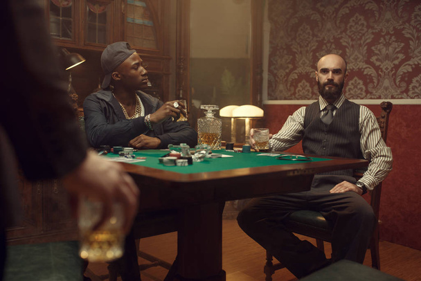 Τρεις παίκτες πόκερ με ουίσκι και πούρα κάθονται στο τραπέζι. Παιχνίδια εθισμού στην τύχη, τυχερά παιχνίδια σπίτι, - Φωτογραφία, εικόνα