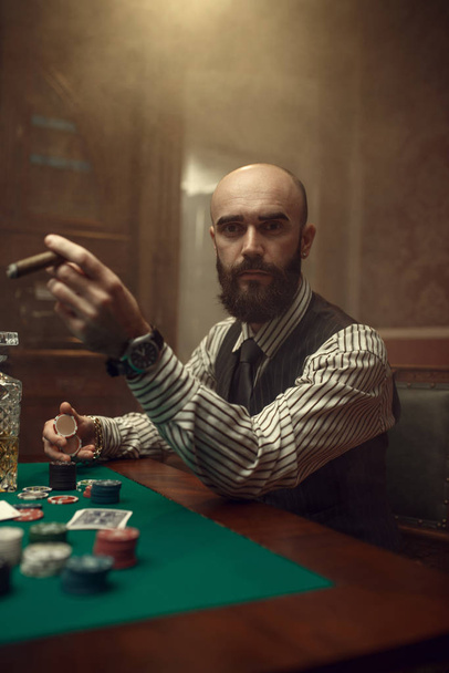 Γενειοφόρος παίκτης πόκερ με πούρο που παίζει στο καζίνο. Παιχνίδια εθισμού στην τύχη. Ο άνθρωπος δελεάζει σε τυχερά παιχνίδια σπίτι - Φωτογραφία, εικόνα