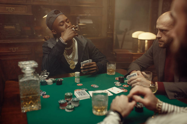 Kolme pelaajaa istuu pelipöydässä vihreällä liinalla kasinolla. Sattumariippuvuuden pelit, uhkapeli talo. Miehet vapaa viskin ja sikarien kanssa
, - Valokuva, kuva