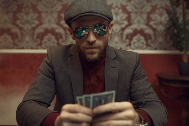 Σοβαρός παίκτης πόκερ σε γυαλιά ηλίου που παίζει στο καζίνο. Παιχνίδια εθισμού στην τύχη. Ο άνθρωπος με τα χαρτιά στα χέρια leisures στο σπίτι τυχερών παιχνιδιών - Φωτογραφία, εικόνα
