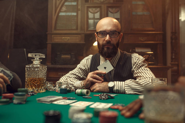 Parrakas pokerinpelaaja näyttää ässän kortin, kasino. Sattumariippuvuuden pelit. Mies vapaa-ajan uhkapeli talo, pelipöytä
 - Valokuva, kuva