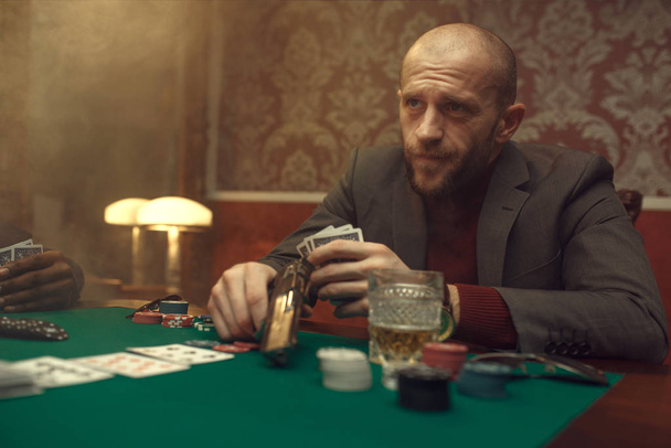 Pokerspieler mit Pistole spielt im Casino, Risiko. Glücksspielsucht. Mann vergnügt sich in Spielothek, Spieltisch mit grünem Tuch - Foto, Bild