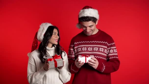 Young european couple with christmas gift box smiling isolated on red background studio. New 2020 year decorations, presents, party, happiness concept. - Video