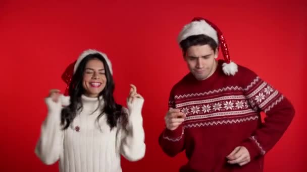 Young couple dancing in Christmas decorations Santa Claus hats on red studio background. Love, holidays, happiness concept. - Кадры, видео